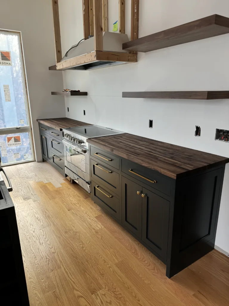 Lower custom kitchen cabinets installed next to a stainless steel range with matching floating wood shelves on the wall.