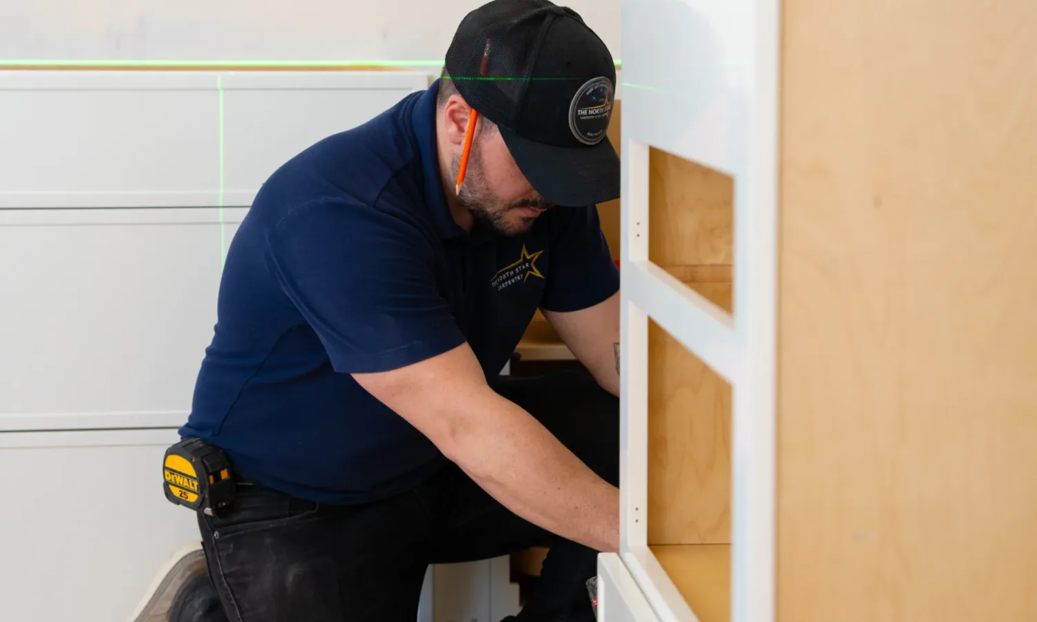 Carpenter aligning Custom Kitchen Cabinets NY using a green precision laser level.